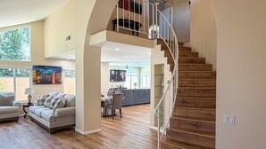 A spacious living area with a wooden staircase, a dining area, and a large window with a cityscape view. - Grill, Large Pool, Plush Patio Furniture, Umbrella (Rancho Cucamonga)
