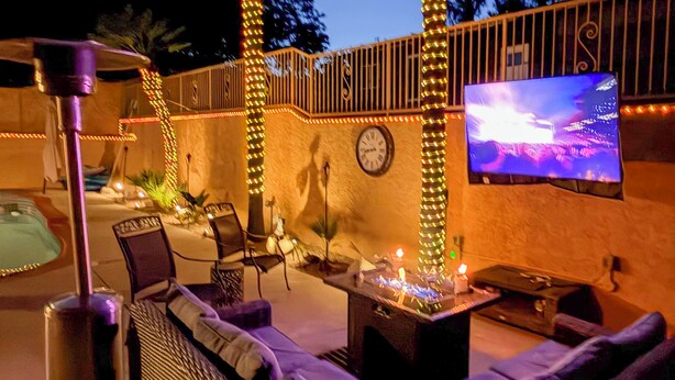 An outdoor patio with a TV, seating, and decorative lights. - Grill, Large Pool, Plush Patio Furniture, Umbrella (Rancho Cucamonga)