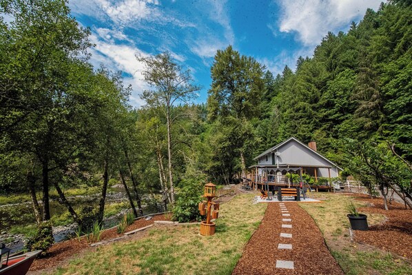 A house with a deck, surrounded by a wooded area and a small stream.