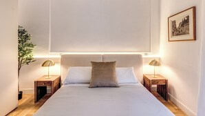 Een keurig opgemaakt slaapkamer met een groot bed, twee nachtkastjes met lampen, een potplant en een ingelijste foto aan de muur.