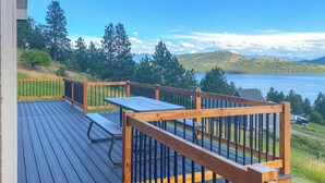 En terrass med ett bord och stolar, med utsikt över en sjö och skogbeklädda kullar.