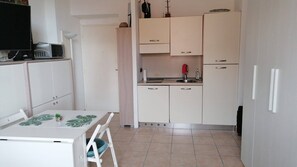 Een kleine keuken met een eettafel, kastjes en een magnetron.