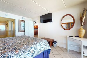 A bedroom with a bed, a TV, a mirror, a desk, and a trash bin. - Luxury Perks, Corner 3BR: Suntide III - Unit 1001 (South Padre Island)