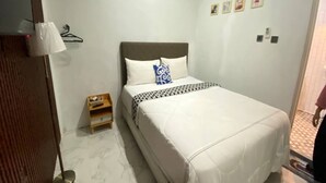A neatly arranged hotel room with a bed, a small wooden nightstand, a wall-mounted lamp, and a door with a towel hanging on it. - Capital O 94840 Unihomestay Malioboro (Yogyakarta)