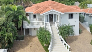 Una casa bianca a due piani con tetto in tegole rosse, un balcone bianco e un vialetto lastricato che conduce all'ingresso.