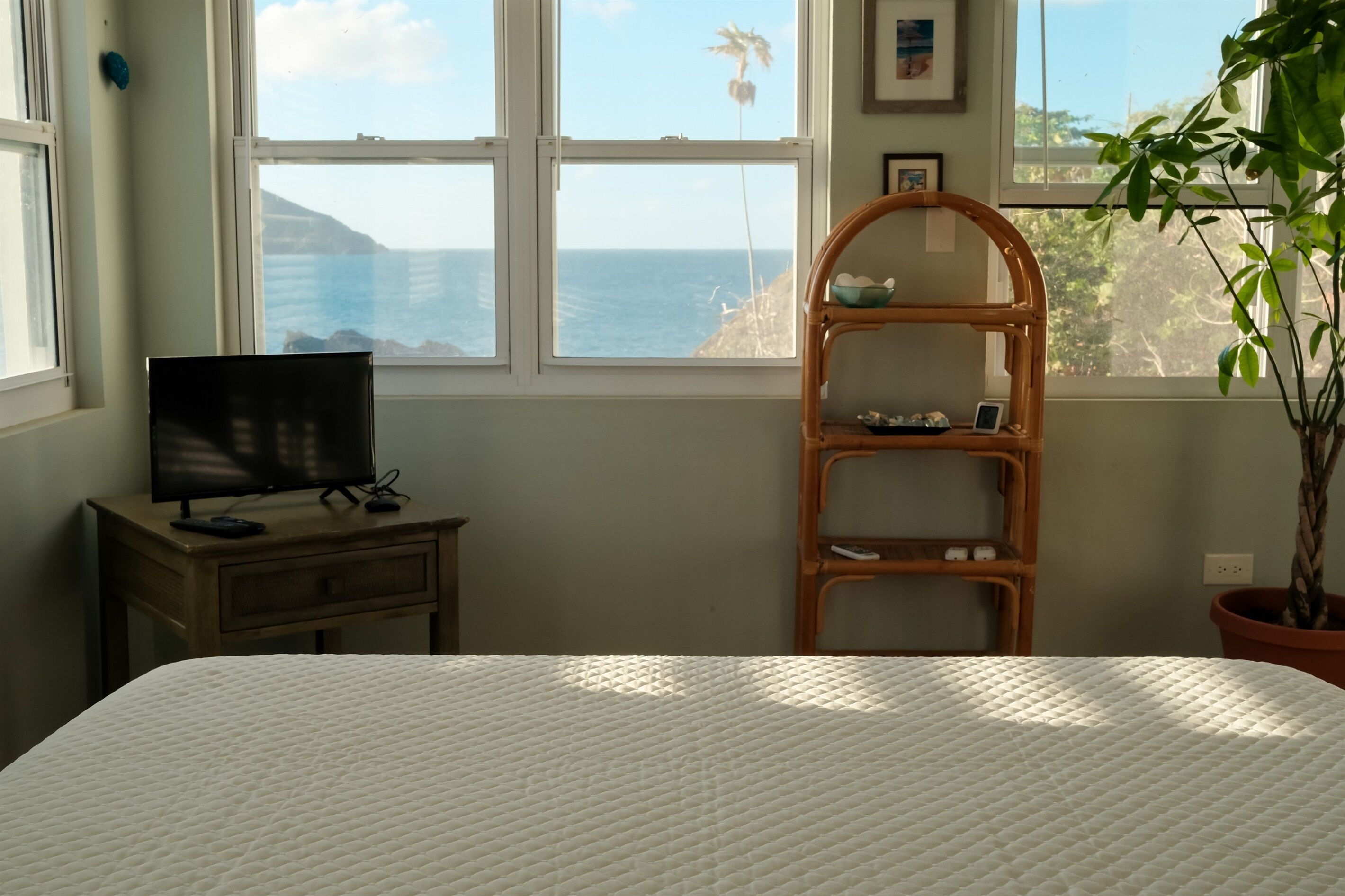 Ein Schlafzimmer mit einem Bett, einem Fernseher auf einem Holztisch, einem Regal und Blick aufs Meer.