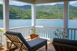 A balcony with two lounge chairs and a potted plant, overlooking a clear blue sea and green hills. - Stunning views + 3 Mins to Hull Bay + Quiet Escape (St. Thomas)