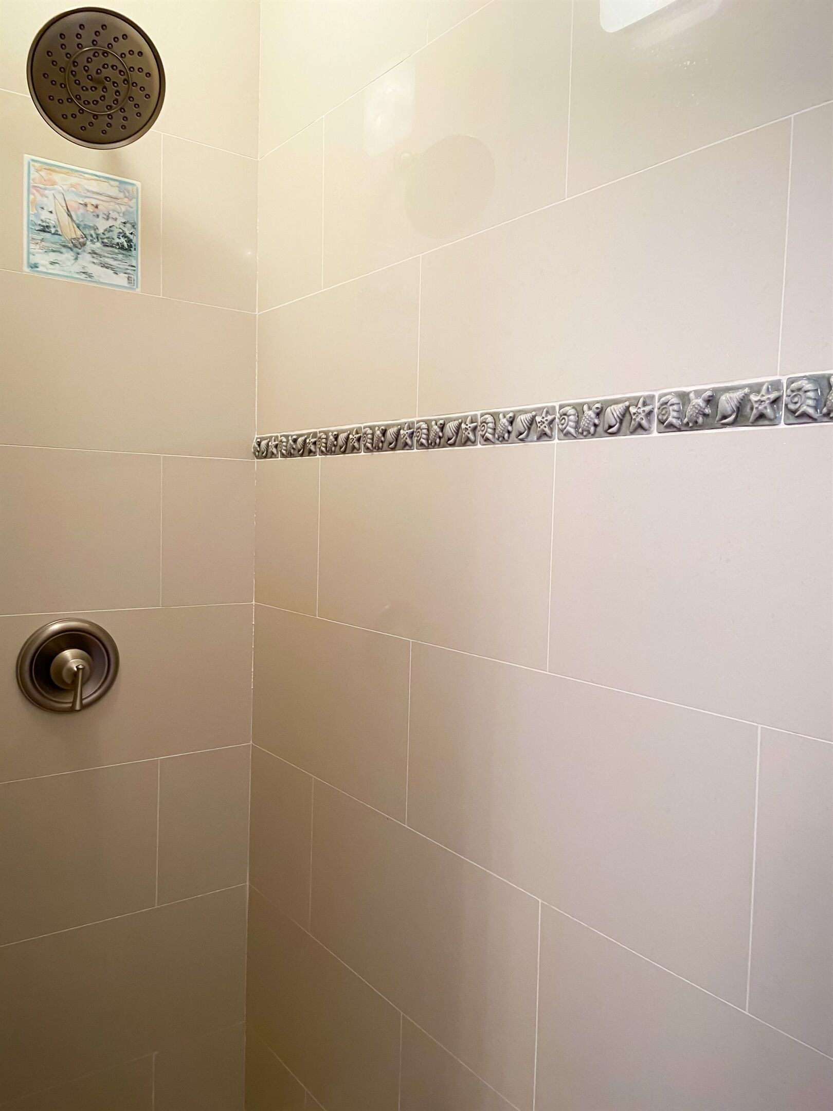 Un espace douche avec des carreaux de couleur beige, une bordure décorative en carreaux et une pomme de douche fixée au mur.