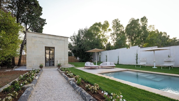 Un área de piscina moderna al aire libre con un edificio de piedra, un camino de grava y un césped bien cuidado.