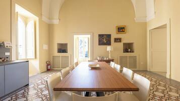 Un comedor amplio con una larga mesa de madera, sillas blancas y baldosas de suelo con diseño.