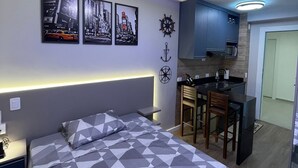 A modern bedroom with a geometric-patterned bed, a small kitchenette, and wall-mounted artwork. - Studio with swimming pool near to the Malls. (Curitiba)