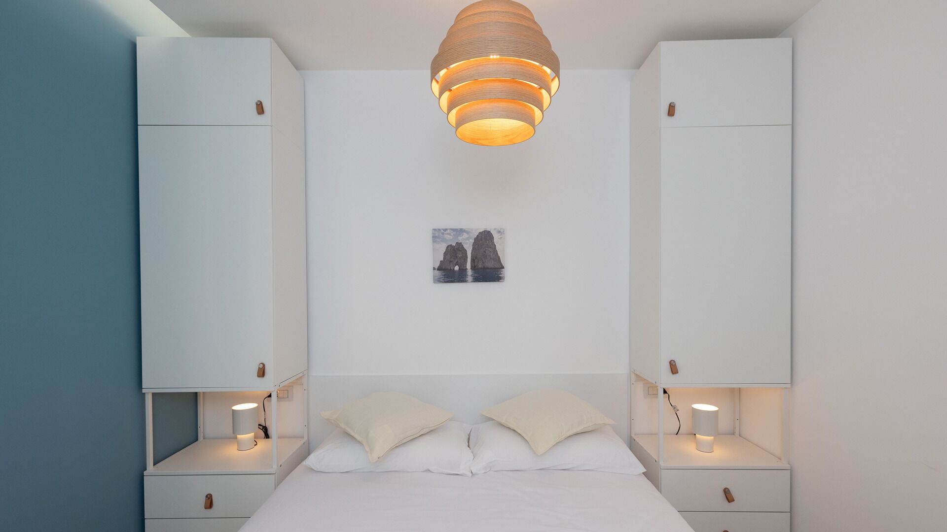 A bedroom with a bed, two nightstands, a hanging light fixture, and a framed picture on the wall.