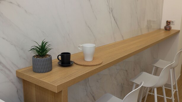 A wooden bar counter with a marble wall backdrop, a potted plant, a black mug, and a white cup. - Bed&Breakfast De Lorenzo 22 (Naples)