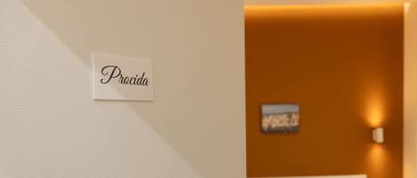 A hotel room with a bed, a wall-mounted sign reading "Procida", and a painting on the wall.
