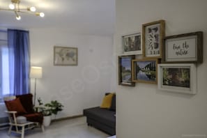 Un soggiorno con un divano, una poltrona, una lampada e quadri appesi al muro.