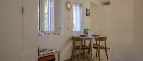 A kitchen with a dining table, chairs, a window, and a shelf with items.