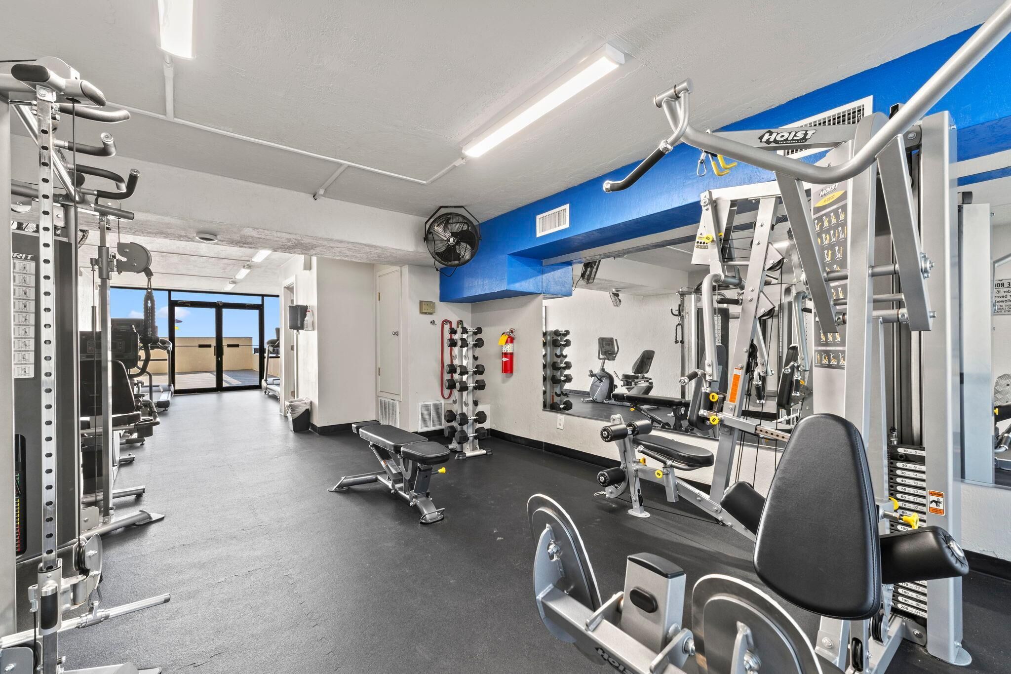 Une salle de sport équipée de divers appareils d’exercice, d’un banc et d’un grand miroir.