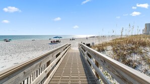 A wooden boardwalk leading to a sandy beach with a clear blue sky. - Island Winds West Unit 575 (Gulf Shores)