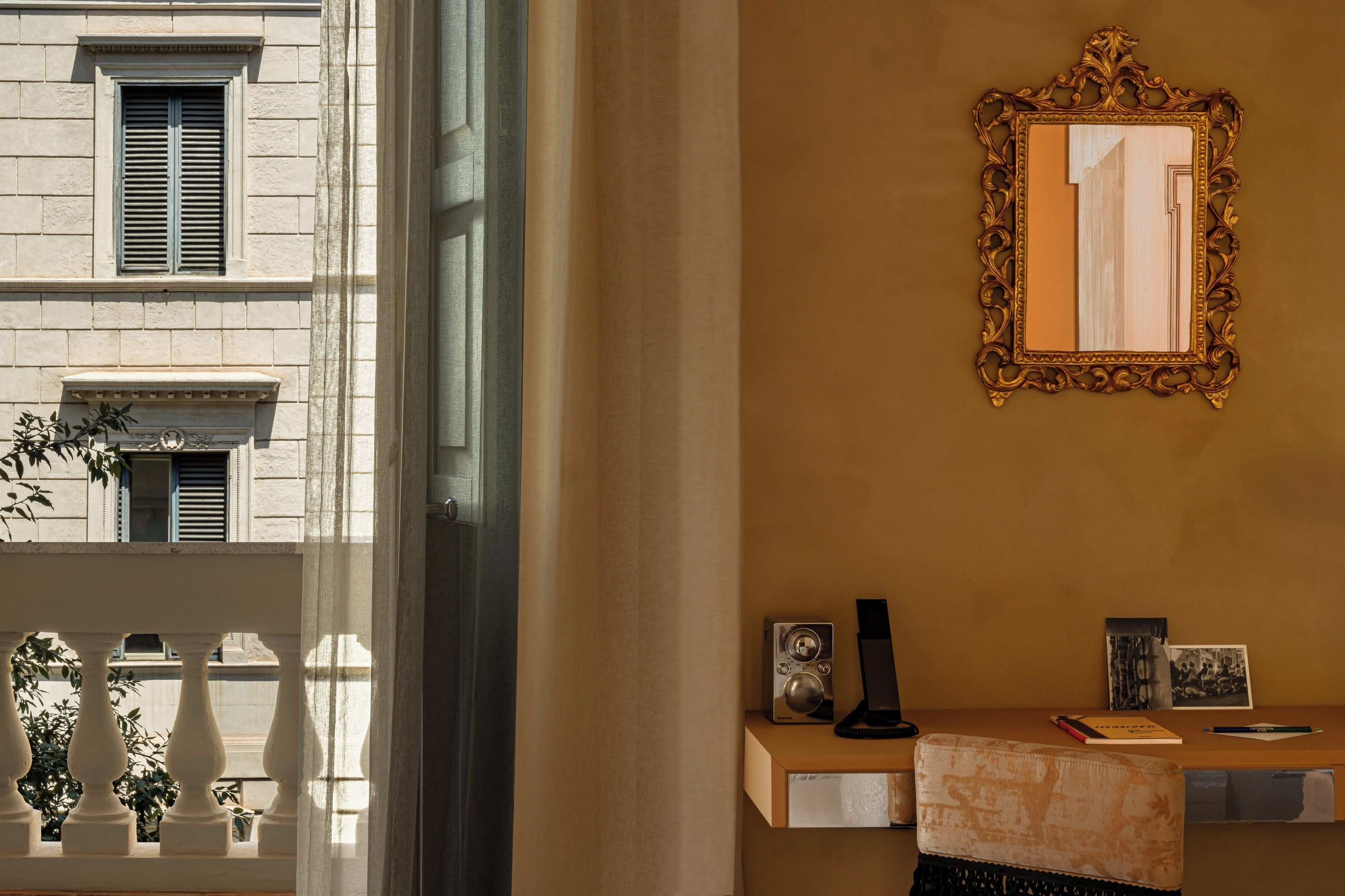 A room with a large window, a mirror, a small table with a lamp, and a plant.
