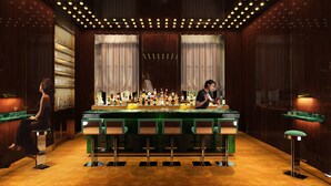 Eine Bar mit grüner Theke, zahlreichen Flaschen und Barhocker.