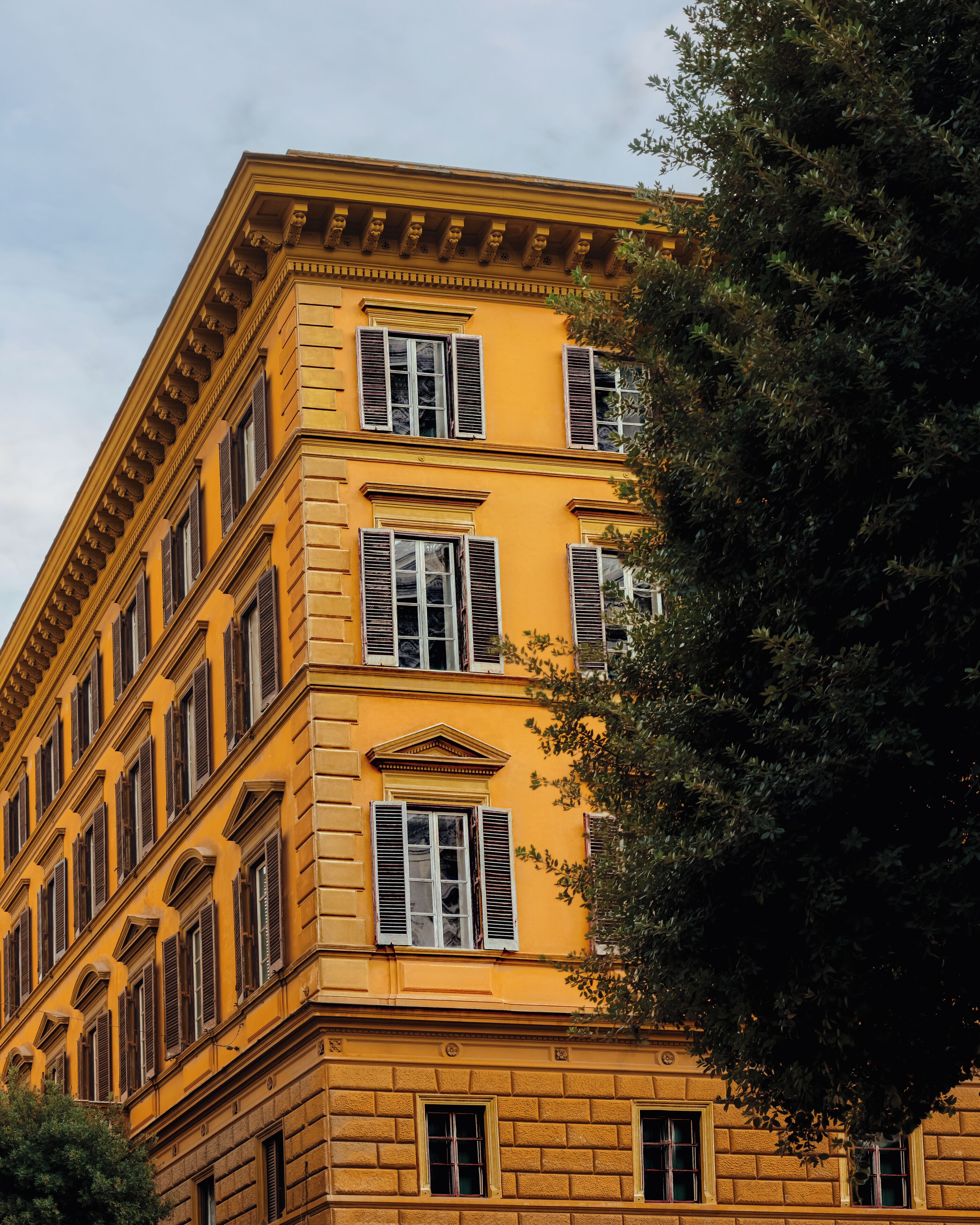 En bygning med flere etager, gul facade, mange vinduer med markiser og klassiske arkitektoniske detaljer.