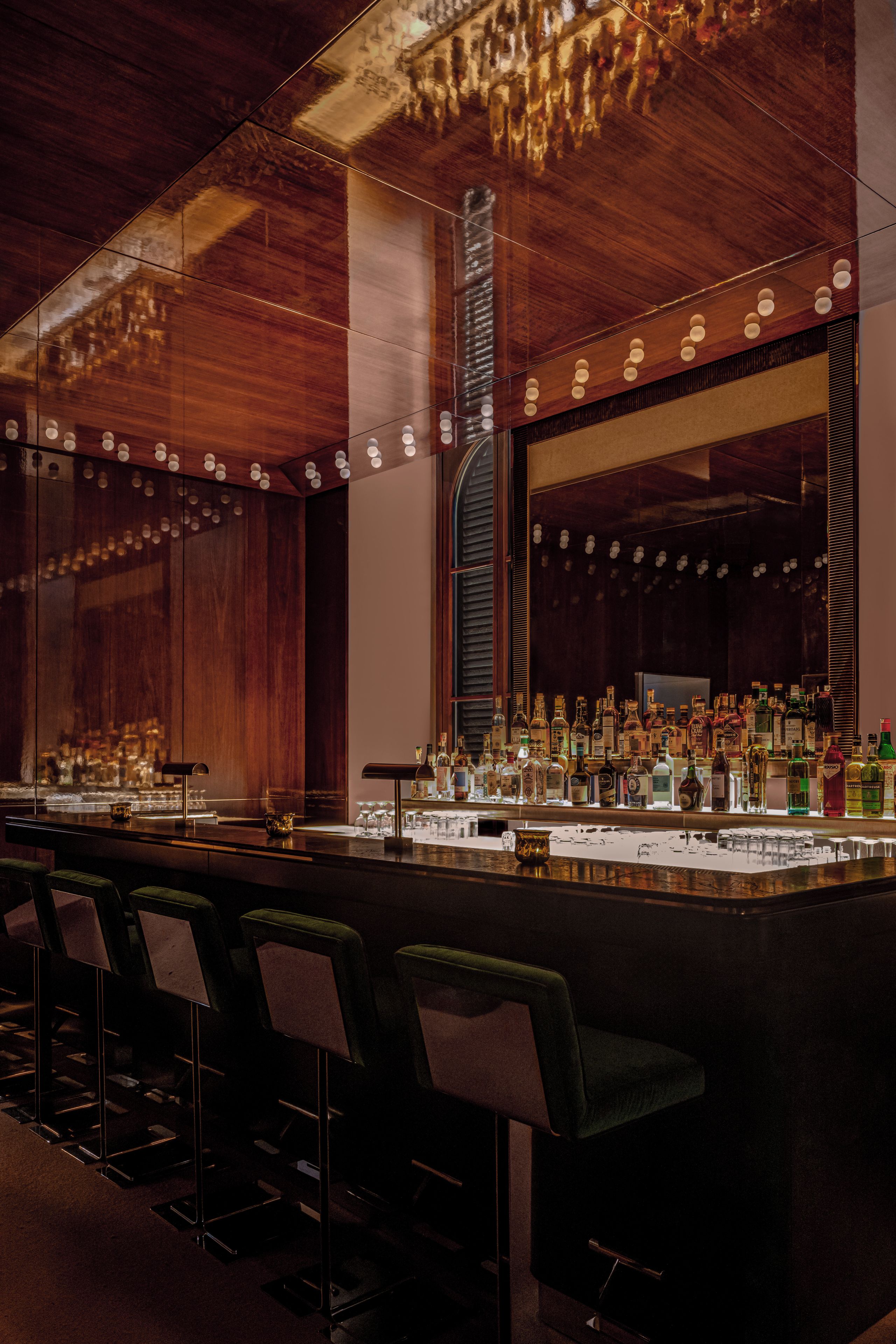 Angolo bar con un lungo bancone, diverse bottiglie di liquore e sgabelli da bar.