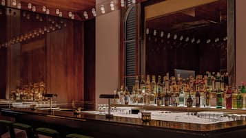 Angolo bar con un lungo bancone, diverse bottiglie di liquore e sgabelli da bar.