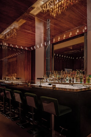 Een bar met een lange toonbank, diverse drankflessen en barstoelen.