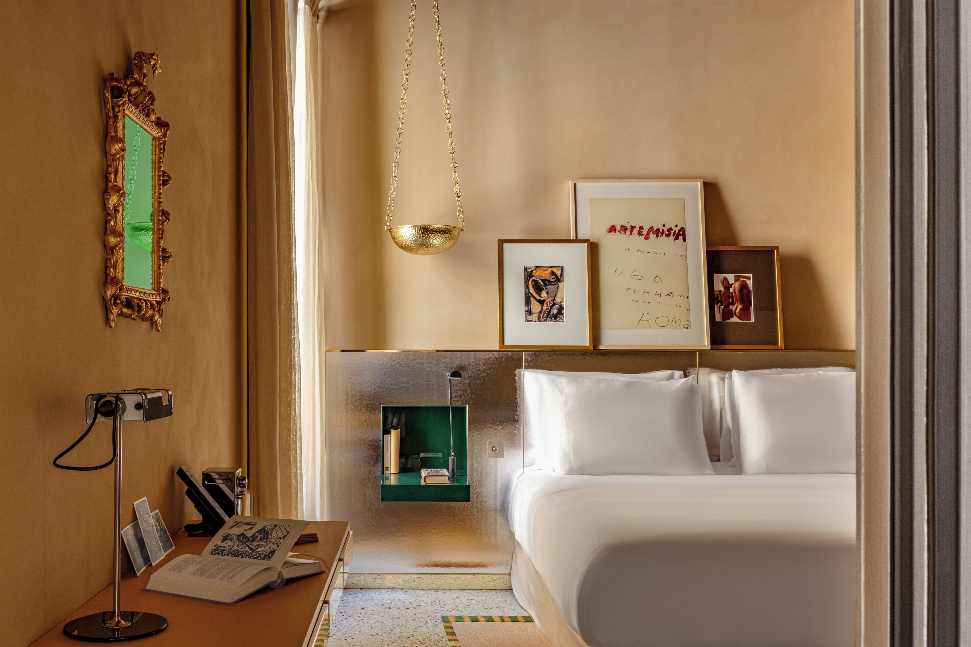 A hotel room with a bed, a desk with a lamp, a framed picture, and a hanging light fixture.
