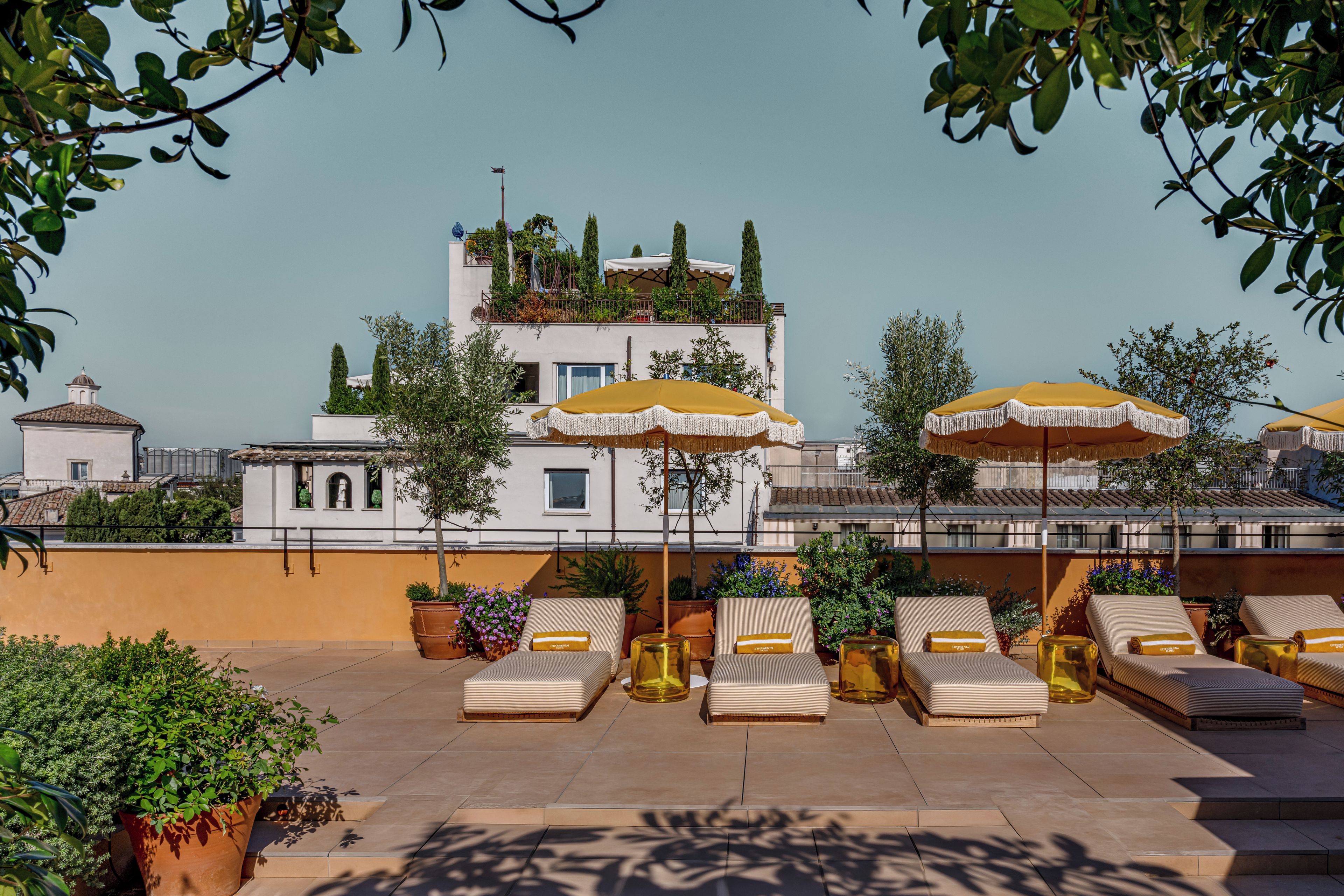 Terraço no telhado com espreguiçadeiras, guarda-sóis amarelos e plantas em vasos.
