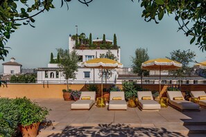 A rooftop terrace with lounge chairs, yellow umbrellas, and potted plants. - Experimental Roma (Rome)