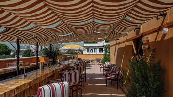 An outdoor bar area with striped awnings, seating, and a view of buildings in the background.