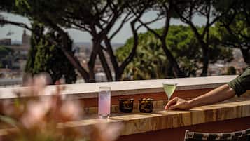 Zona de bar con vistas al paisaje urbano, una copa de bebida y una persona alcanzando un cóctel.
