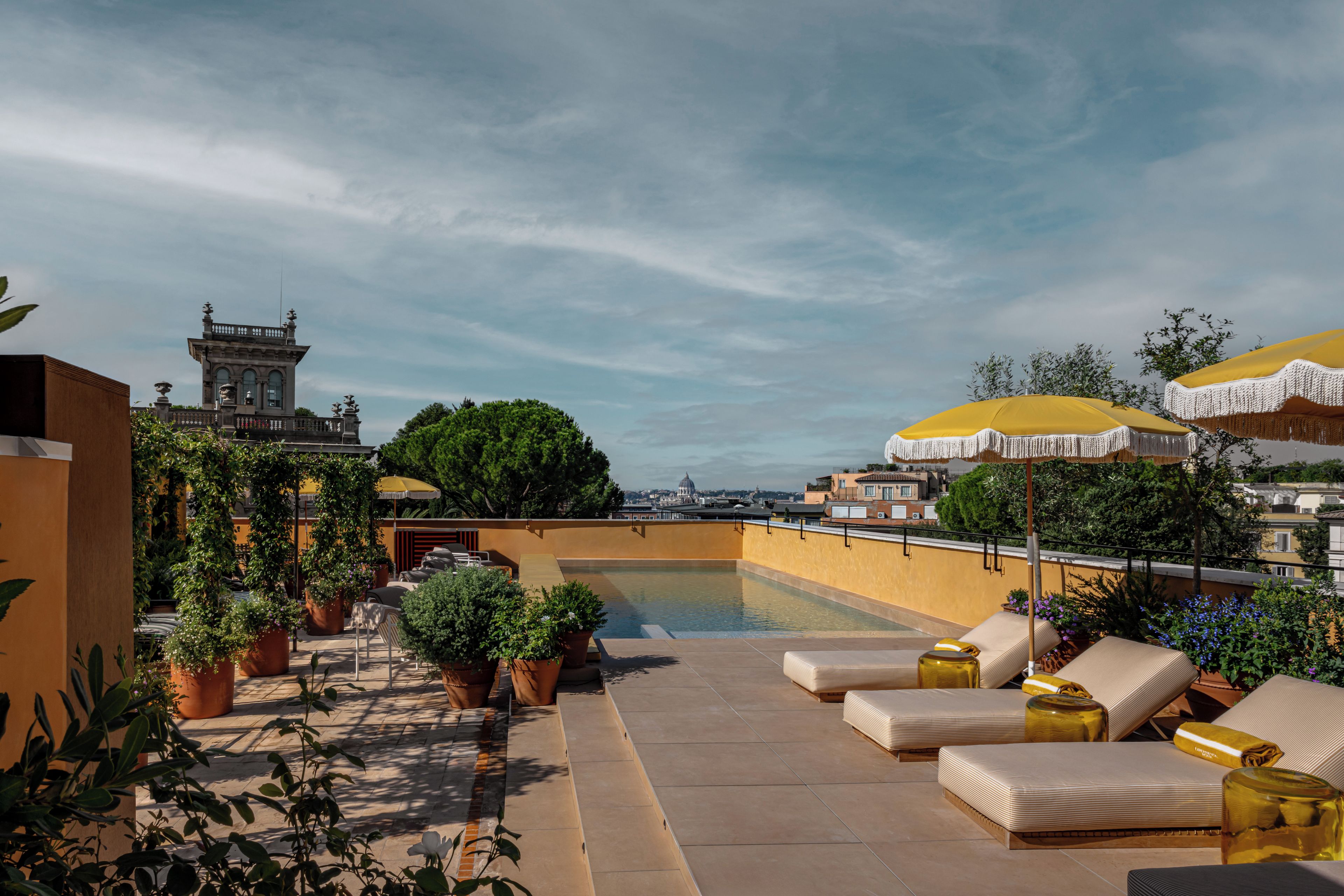 A rooftop terrace with a swimming pool, outdoor seating, and a view of a historic building.