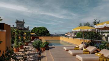 A rooftop terrace with a swimming pool, outdoor seating, and a view of a historic building.