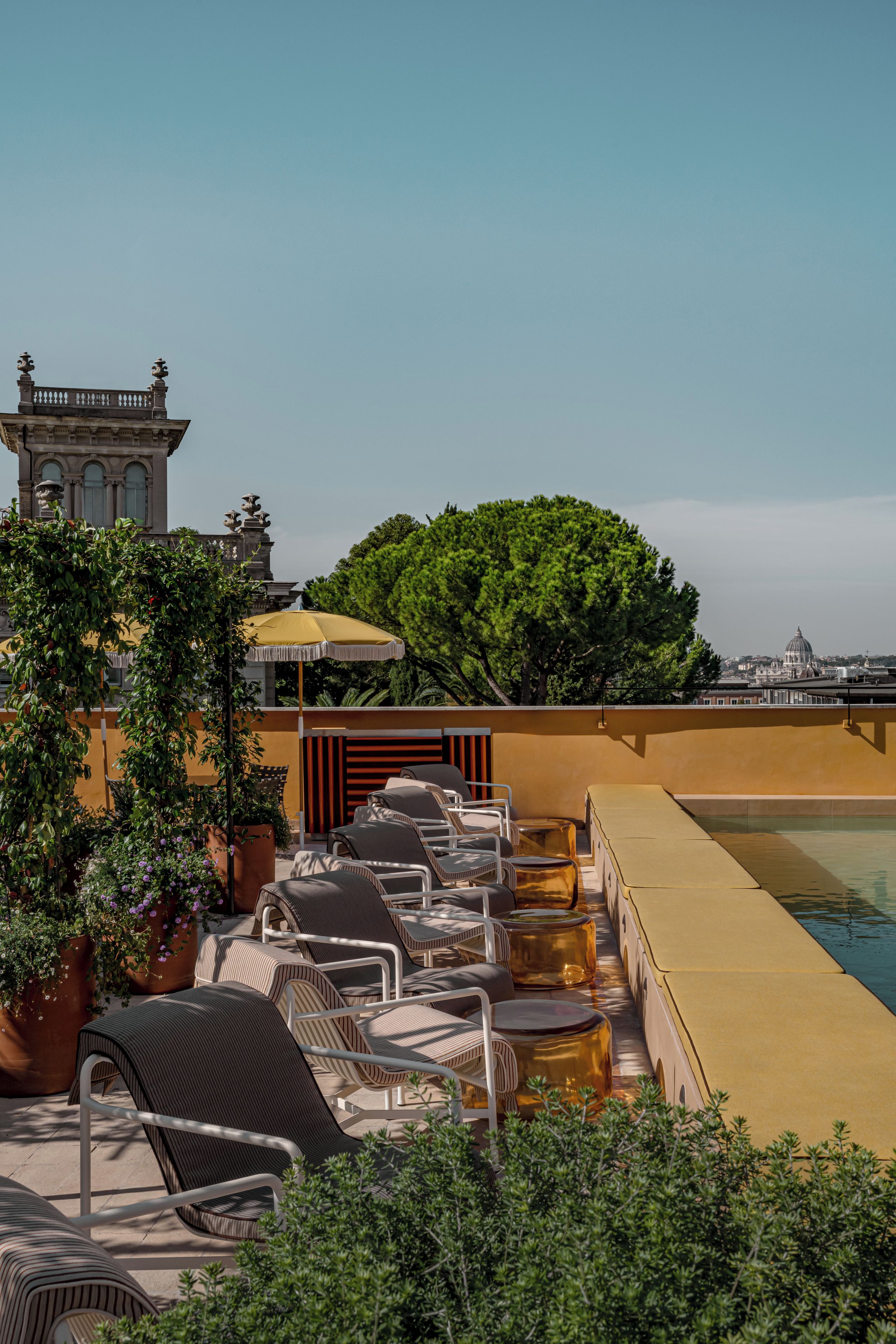 Área de piscina no terraço com espreguiçadeiras e vista para um edifício histórico.
