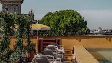 Área de piscina no terraço com espreguiçadeiras e vista para um edifício histórico.