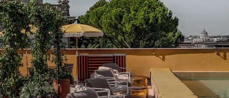 Un área de piscina en la azotea con sillones reclinables y vista a un edificio histórico.