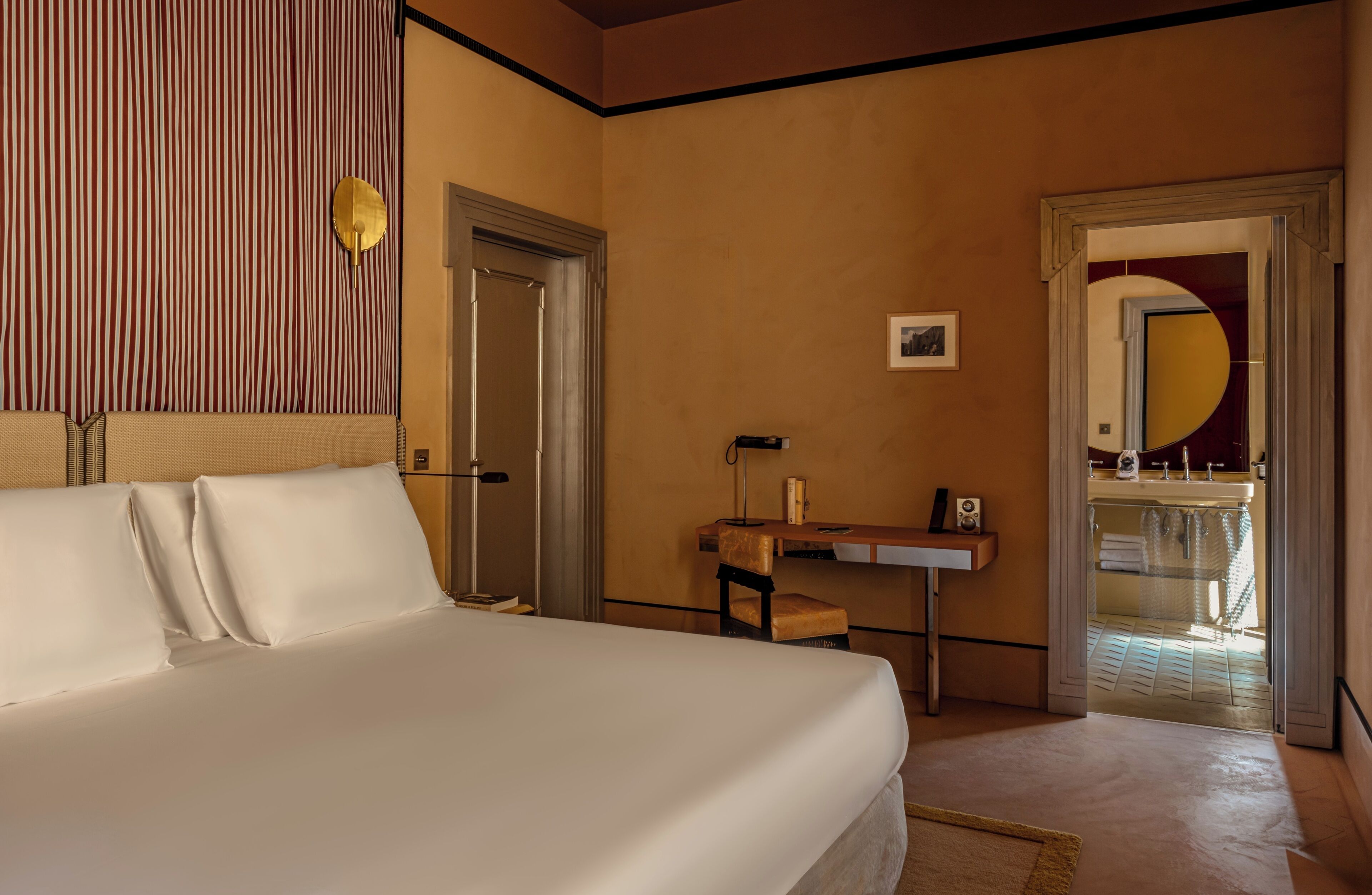 A hotel room with a bed, a desk, a chair, a mirror, and a door.