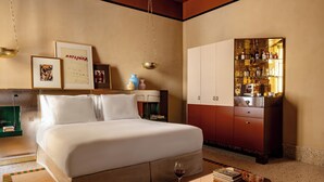 A hotel room with a bed, a minibar, a bookshelf, and a coffee table with books and a wine glass. - Experimental Roma (Rome)