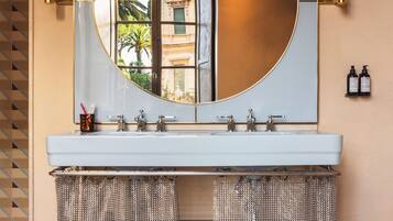 A bathroom with a round mirror, a white sink, two chain-link trash bins, and a patterned floor.