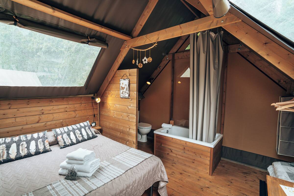 A cozy, wooden interior with a bed, a bathroom, and a window.