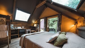 A cozy bedroom with a large bed, a wooden dresser, a desk with a chair, and a window overlooking greenery. - GLAMPING PIAN DELLE GINESTRE (Sassetta)
