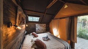 A cozy room with wooden walls, a bed with a quilt and pillows, a window with curtains, and a skylight. - GLAMPING PIAN DELLE GINESTRE (Sassetta)