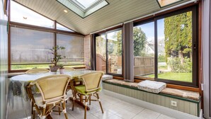 A dining area with a table and chairs, large windows with blinds, a skylight, and a view of a garden. - Comfortable Cottage Between Land and Sea with Wi-Fi in Pont-Aven (Pont-Aven)