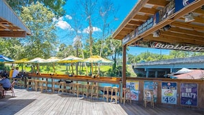 Ein Außenbereich mit Bar, Holzboden, Barhocker und Sonnenschirmen.