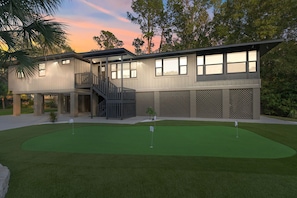 Une maison moderne à deux étages, dotée d’un patio couvert, d’une petite pelouse et d’un espace dédié à l’entraînement au golf.