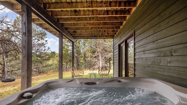 A hot tub under a wooden pergola with a view of a grassy area and trees. - Deadwood Pines Hideaway (Sturgis)