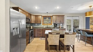 A modern kitchen with wooden cabinets, stainless steel appliances, and a central island with chairs. - Deadwood Pines Hideaway (Sturgis)