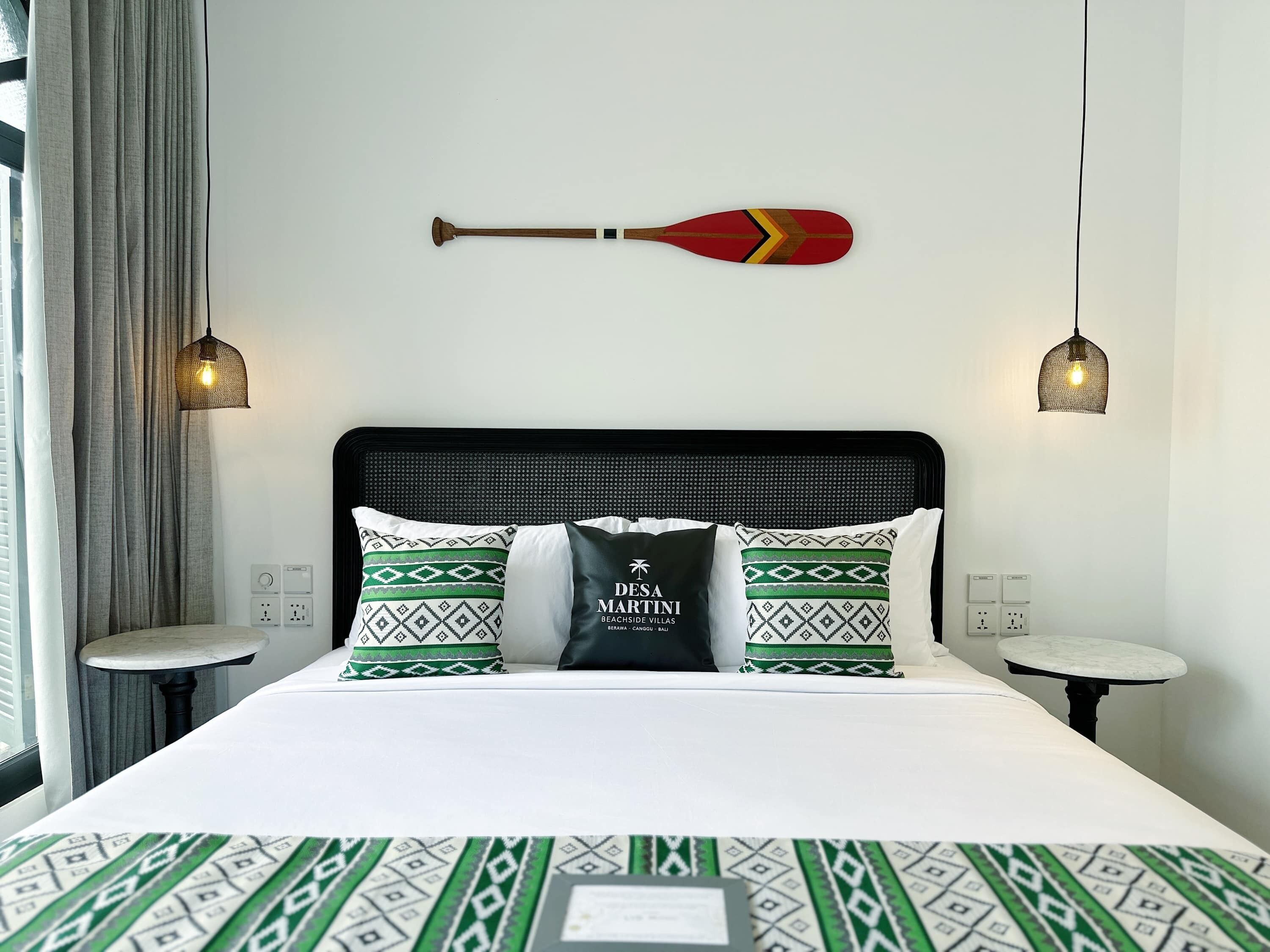 Ein Hotelzimmer mit einem Bett, zwei Kissen, einem Deko-Paddel, zwei Pendelleuchten und einem Nachttisch.